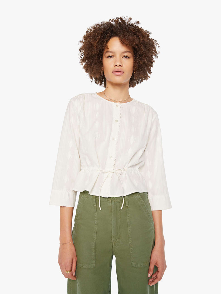 Front view of woman in a white 3/4-length sleeves blouse, a tied waist, buttons down the front and a slightly cropped fit.