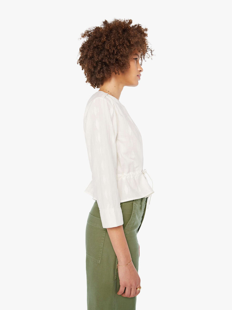 Side view of woman in a white 3/4-length sleeves blouse, a tied waist, buttons down the front and a slightly cropped fit.