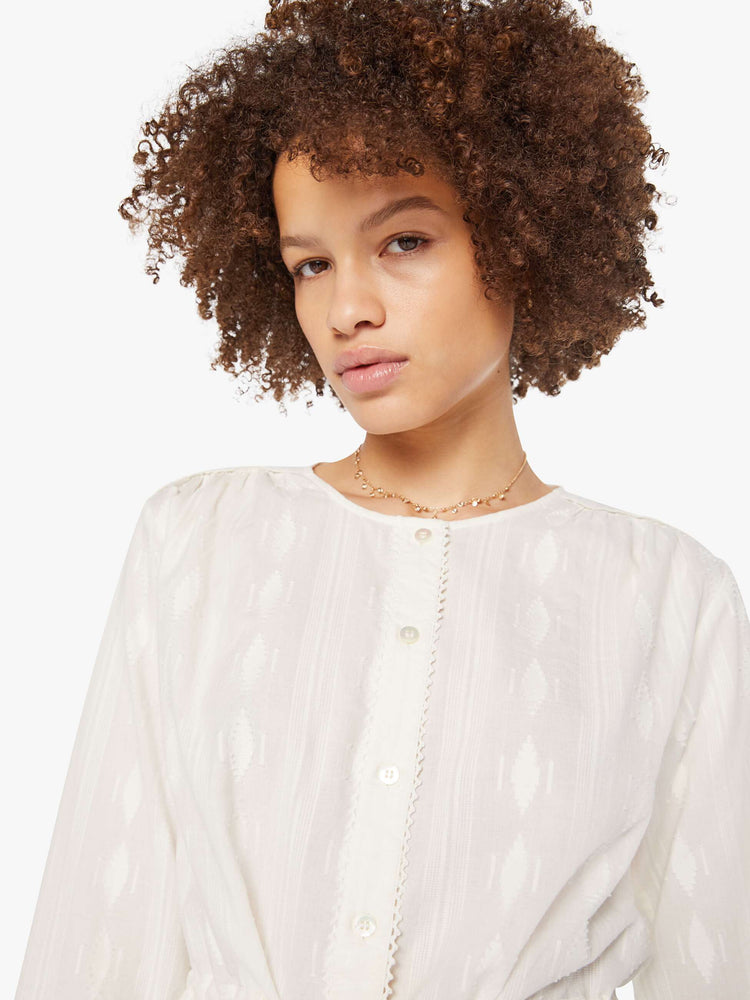 Close up view of woman in a white 3/4-length sleeves blouse, a tied waist, buttons down the front and a slightly cropped fit.