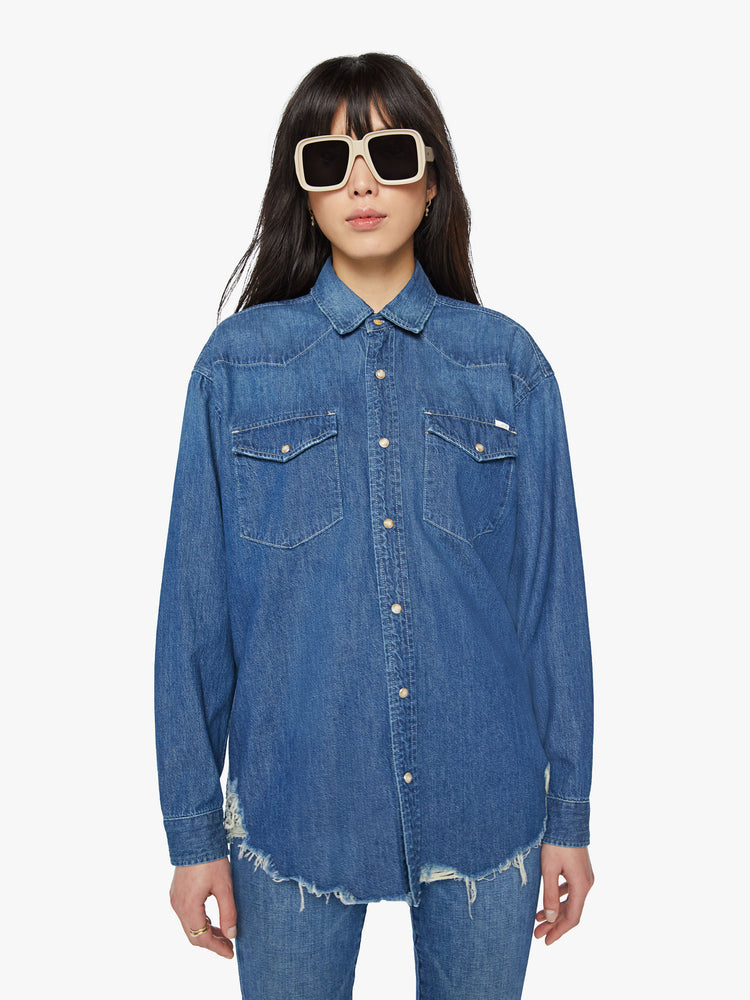 Front view of a woman oversized western inspired denim button-up with front patch pockets and a raw, curved hem in a vintage blue wash.