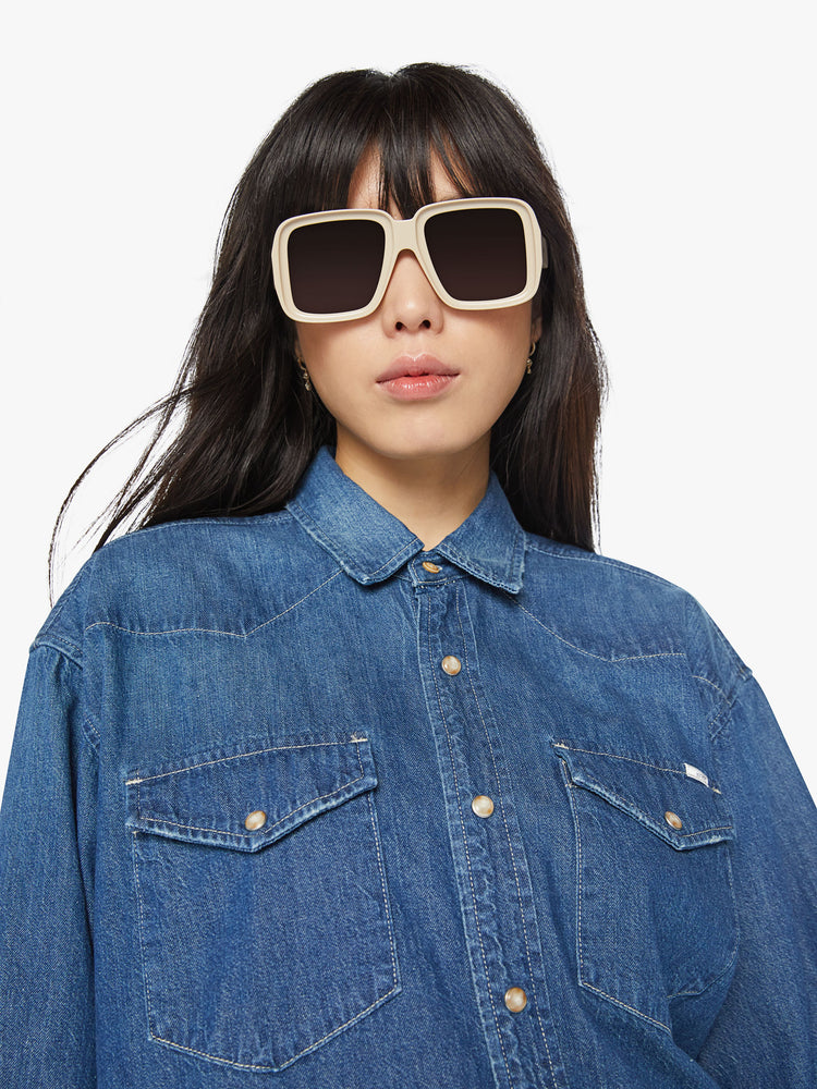 Close up view of a woman oversized western inspired denim button-up with front patch pockets and a raw, curved hem in a vintage blue wash.