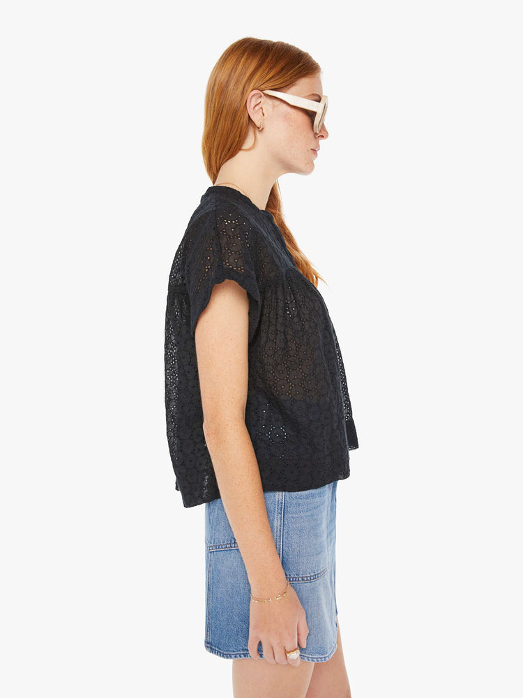 Side view of a woman black lightweight blouse with a buttoned V-neck, short boxy sleeves and ruffles across the chest for a loose, flowy fit.