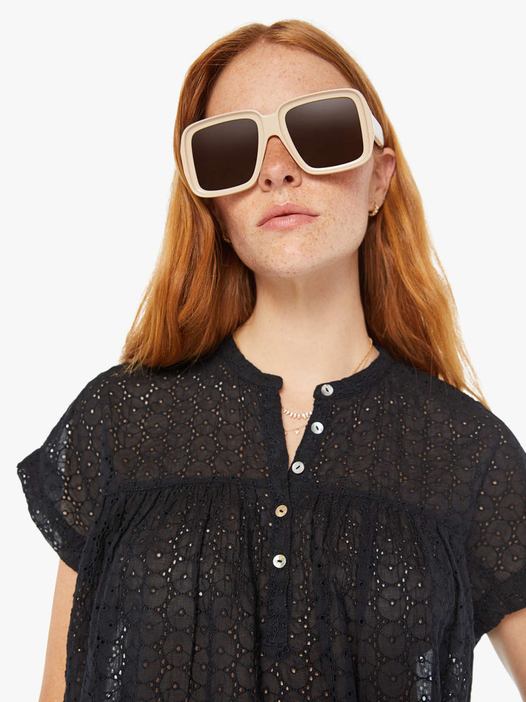 Close up view of a woman black lightweight blouse with a buttoned V-neck, short boxy sleeves and ruffles across the chest for a loose, flowy fit.