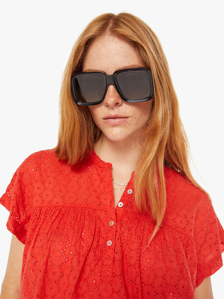 Close up view of a woman red lightweight blouse with a buttoned V-neck, short boxy sleeves and ruffles across the chest for a loose, flowy fit.