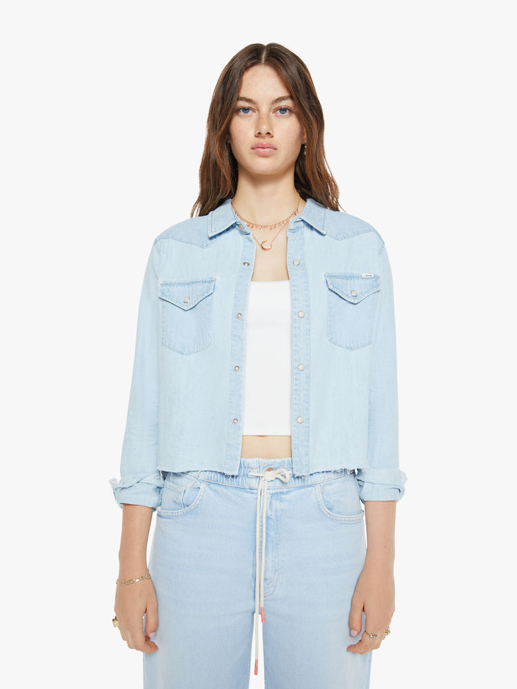 Front view of a woman in a denim button-up with front patch pockets and a cropped, raw hem.