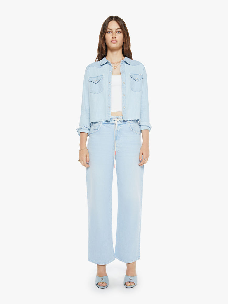 Full body view of a woman in a denim button-up with front patch pockets and a cropped, raw hem.