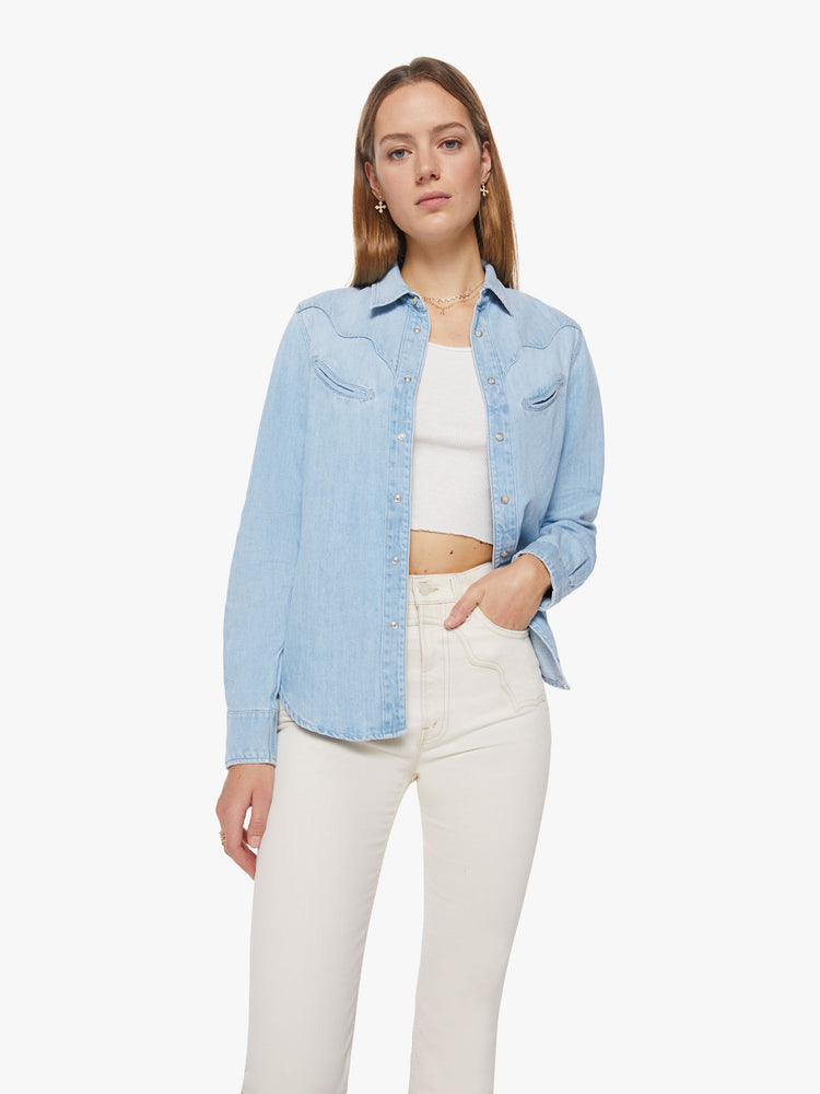 Front view of a woman denim button-up with rounded pockets, yoke detailing, slightly puffed sleeves and a curved hem in a light blue wash.