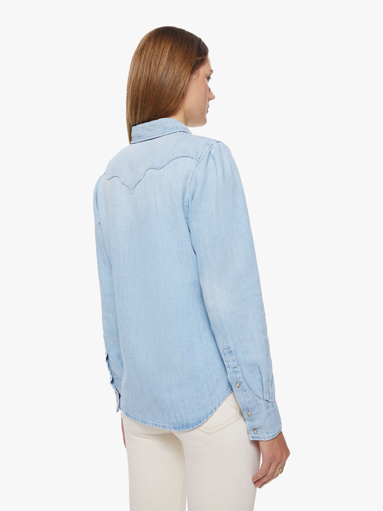 Back view of a woman denim button-up with rounded pockets, yoke detailing, slightly puffed sleeves and a curved hem in a light blue wash.