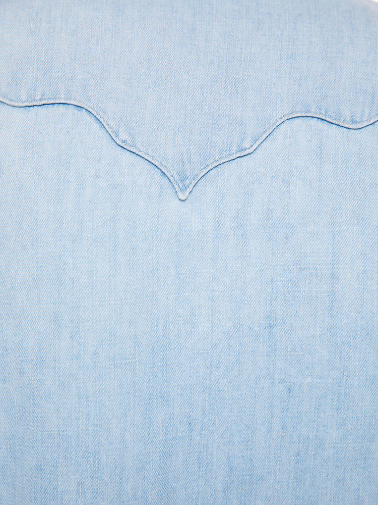 Swatch view of a woman denim button-up with rounded pockets, yoke detailing, slightly puffed sleeves and a curved hem in a light blue wash.