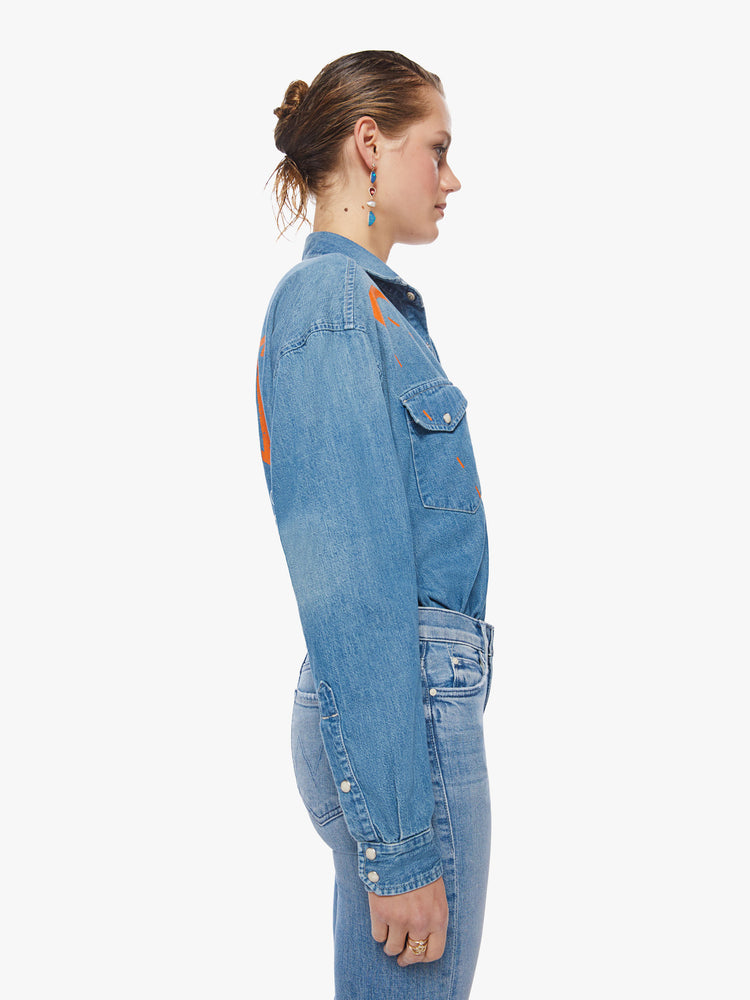 Side view of a woman western-inspired button-upwith drop shoulders, front patch pockets and a slightly oversized fit with subtle fading and orange graphics that channel the electrifying spirit of the tour.