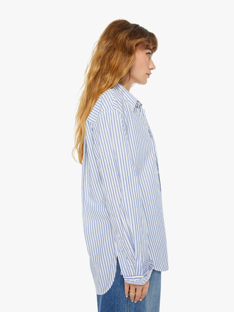 Side view of a woman oversized button-up is designed with long sleeves, drop shoulders, oversized patch pockets, and a curved hem.