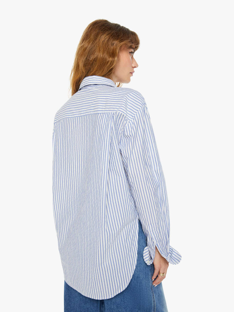Back view of a woman oversized button-up is designed with long sleeves, drop shoulders, oversized patch pockets, and a curved hem.