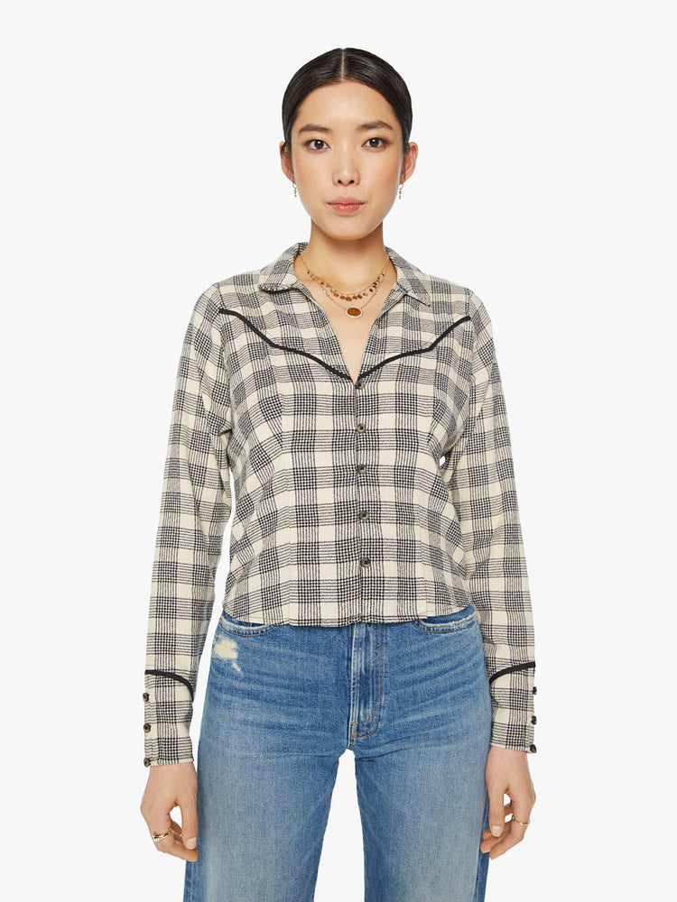 Front view of a woman western inspired button-up with a V-neck, yolk detailing, buttons at the wrists and a slightly cropped hem in black and white plaid print.