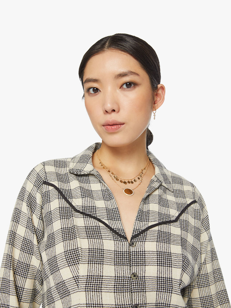 Close up view of a woman western inspired button-up with a V-neck, yolk detailing, buttons at the wrists and a slightly cropped hem in black and white plaid print.