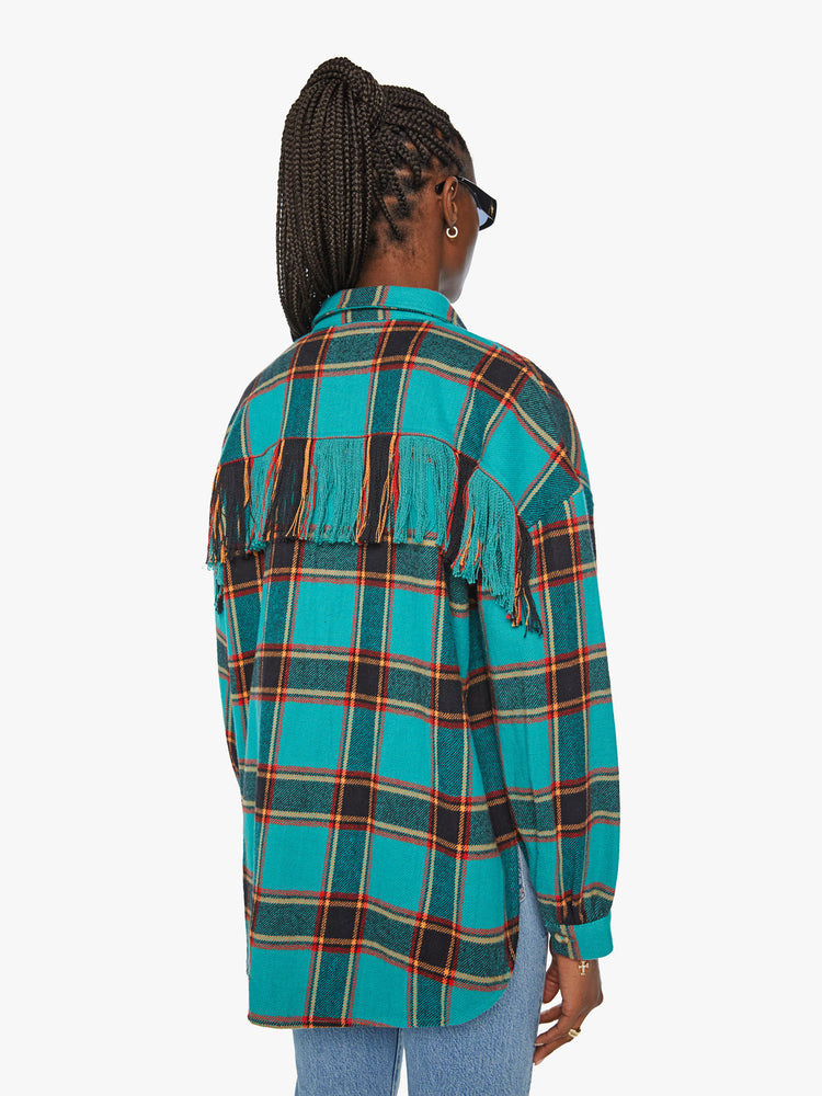 Back view of a woman western inspired button-up with drop shoulders, a curved hem and fringe across the chest and back in a bright blue, red and yellow plaid paint.