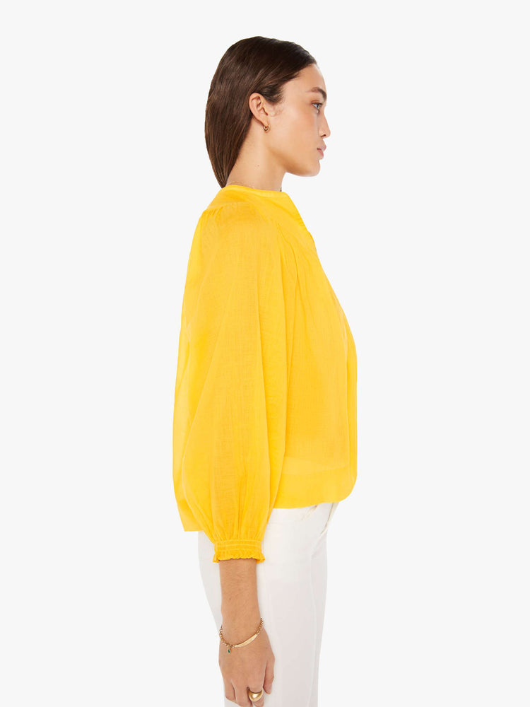 Side view of a woman bright yellow lightweight blouse with a buttoned V-neck, 3/4-sleeves, a slightly cropped hem and ruffles across the chest.