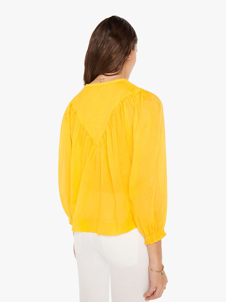 Back view of a woman bright yellow lightweight blouse with a buttoned V-neck, 3/4-sleeves, a slightly cropped hem and ruffles across the chest.