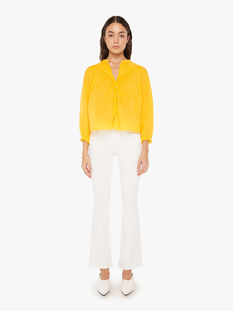 Full body view of a woman bright yellow lightweight blouse with a buttoned V-neck, 3/4-sleeves, a slightly cropped hem and ruffles across the chest.
