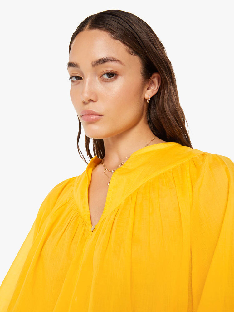 Close up view of a woman bright yellow lightweight blouse with a buttoned V-neck, 3/4-sleeves, a slightly cropped hem and ruffles across the chest.