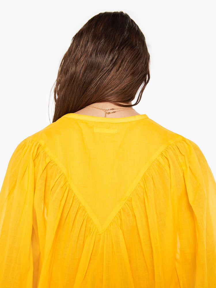 Back  close up view of a woman bright yellow lightweight blouse with a buttoned V-neck, 3/4-sleeves, a slightly cropped hem and ruffles across the chest.