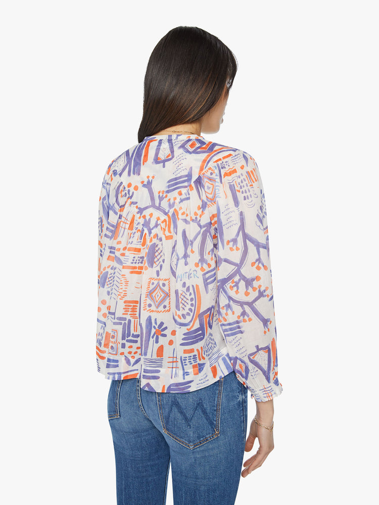 Back view of a woman flowy blouse with a V-neck, cropped balloon sleeves, buttons down the front and ruffles throughout for a loose fit in off white doodles in red and blue.
