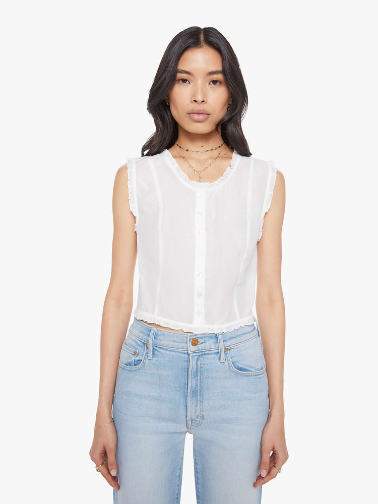 Front view of woman in a sheer white sleeveless scoop neck blouse with ruffled hems, seamed details, buttons down the front and a cropped fit.