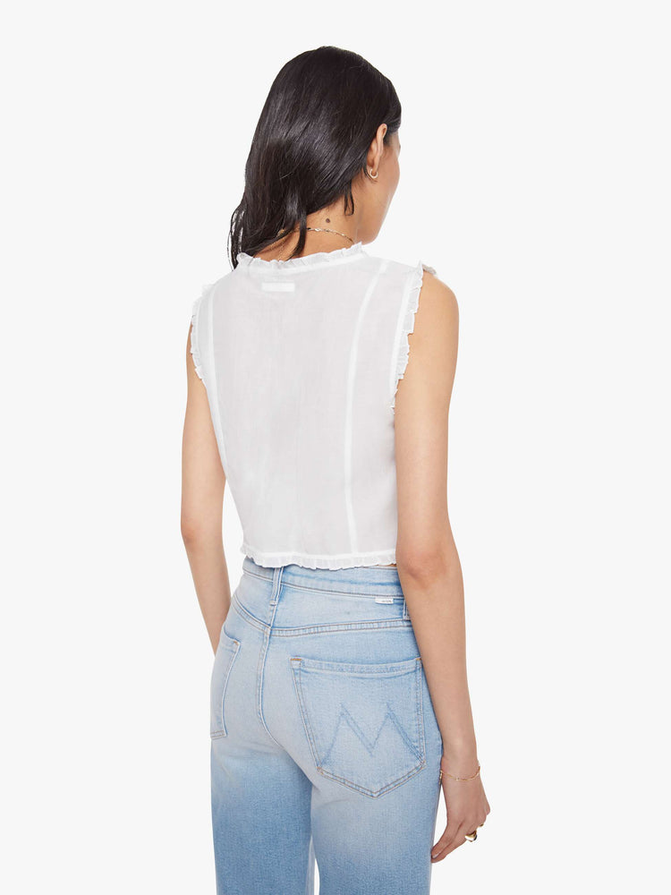 Back view of woman in a sheer white sleeveless scoop neck blouse with ruffled hems, seamed details, buttons down the front and a cropped fit.