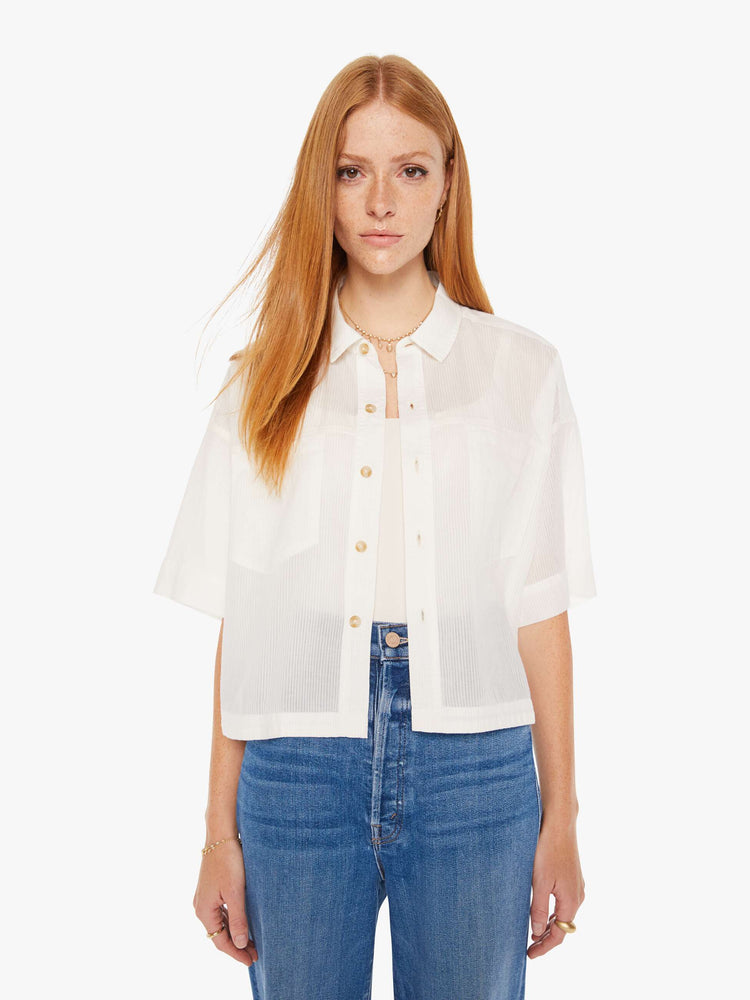 Front view of a womens white button down shirt in a slightly sheer fabric, featuring a cropped boxy fit.