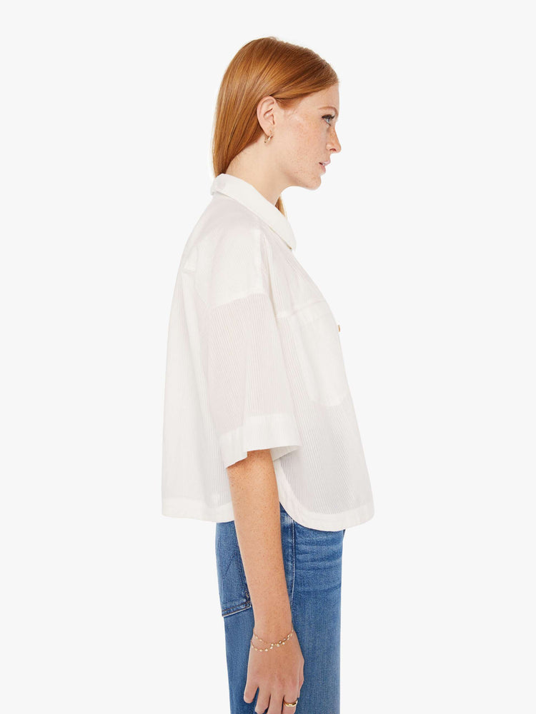 Side view of a womens white button down shirt in a slightly sheer fabric, featuring a cropped boxy fit.
