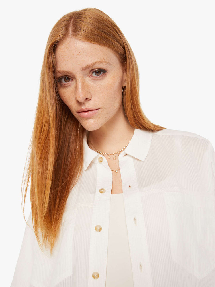 Front close up view of a womens white button down shirt in a slightly sheer fabric, featuring a cropped boxy fit.