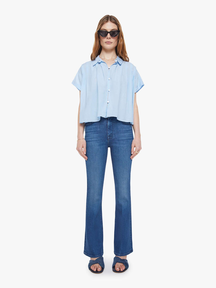 Full body view of a woman in a baby blue boxy short-sleeved button-up with drop shoulders, pleats across the chest and back and a cropped hem.