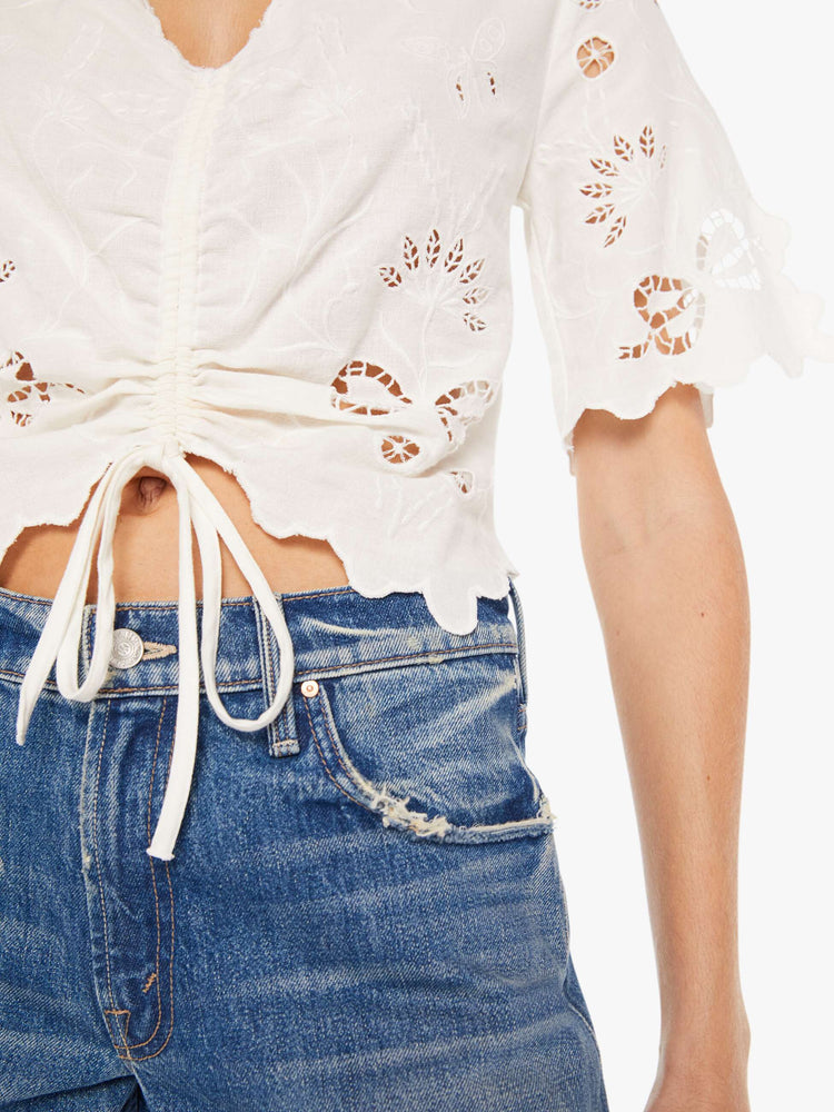 Front close up view of a womens white blouse featuring eyelet and embroidery details and a cinched center.
