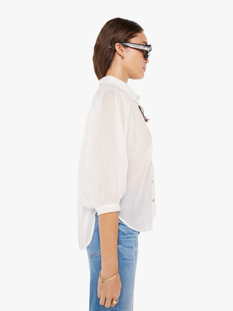 Side view of a woman white lightweight collared blouse with 3/4-length balloon sleeves, a curved hem and ruffles throughout for a flowy fit.