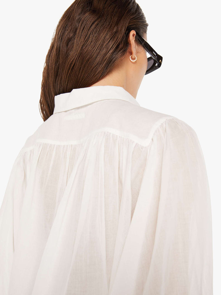 Back close up view of a woman white lightweight collared blouse with 3/4-length balloon sleeves, a curved hem and ruffles throughout for a flowy fit.