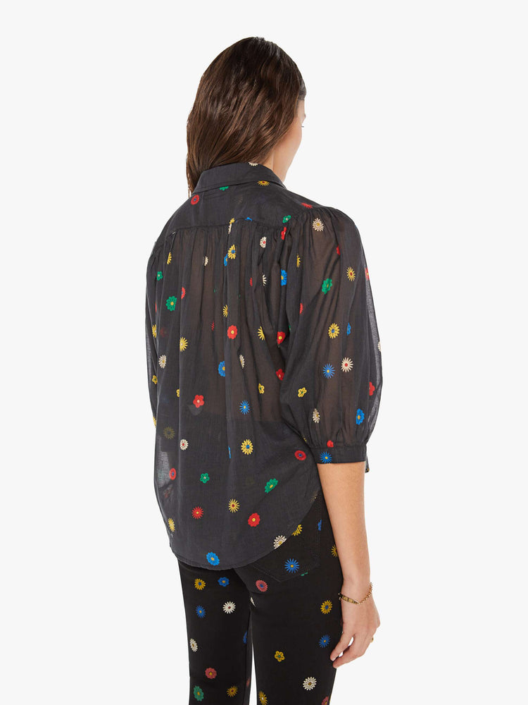 Back view of a woman in a black with colorful daisy print lightweight midi skirt with an elastic drawstring waistband and a ruffled tier for a loose, flowy fit.