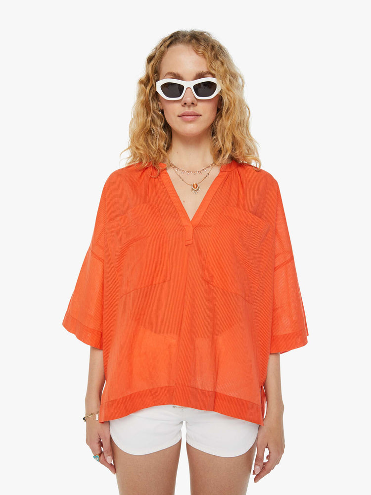 Front view of a woman in a sheer orange V-neck top with oversized patch pocket at the chest.