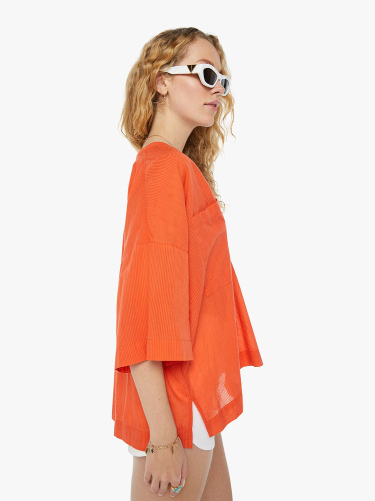 Side view of a woman in a sheer orange V-neck top with oversized patch pocket at the chest.
