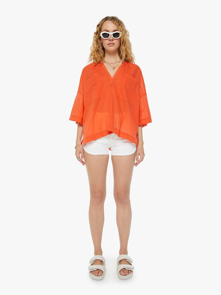 Full front view of a woman in a sheer orange V-neck top with oversized patch pocket at the chest.