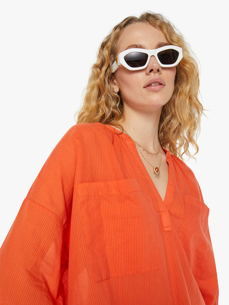 Detailed view view of a woman in a sheer orange V-neck top with oversized patch pocket at the chest.