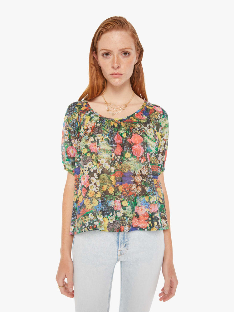 Front view of a woman wearing a sheer peasant blouse featuring a colorful garden print, paired with a light blue wash jean.