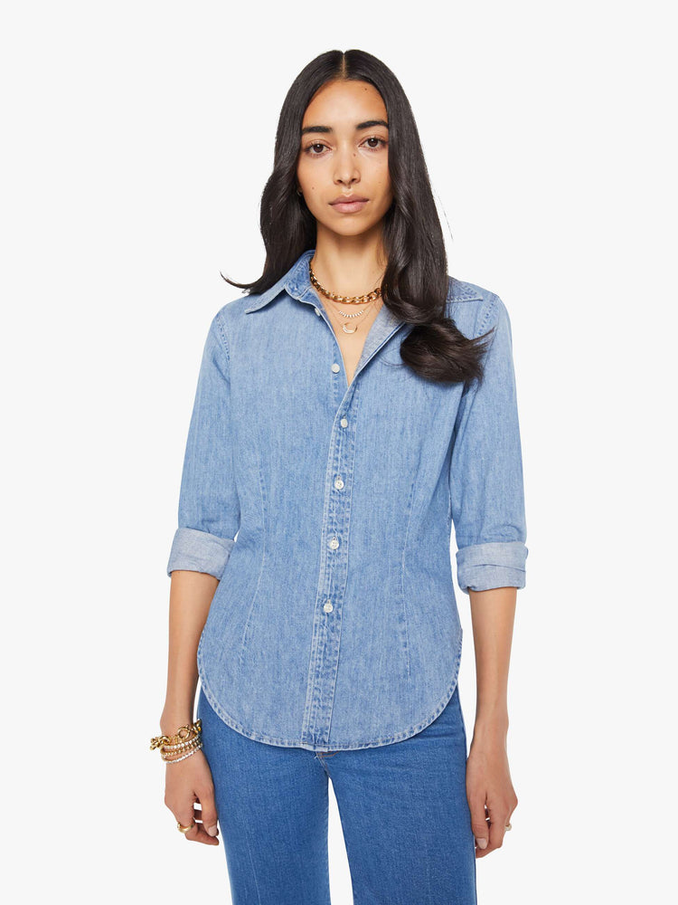 Front view of a woman in a light blue denim button-up features curved hems and seamed details for a more narrow fit.