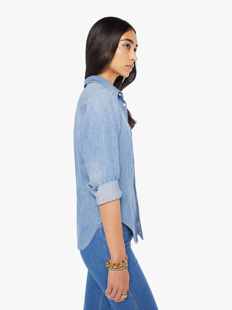 Side view of a woman in a light blue denim button-up features curved hems and seamed details for a more narrow fit.