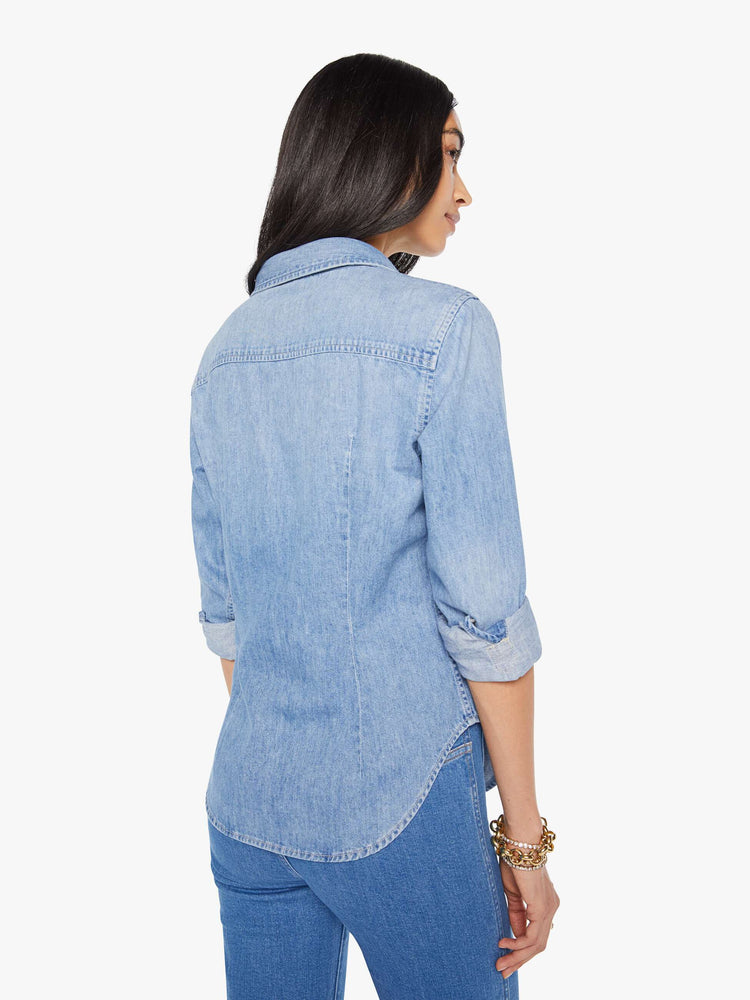 Back view of a woman in a light blue denim button-up features curved hems and seamed details for a more narrow fit.