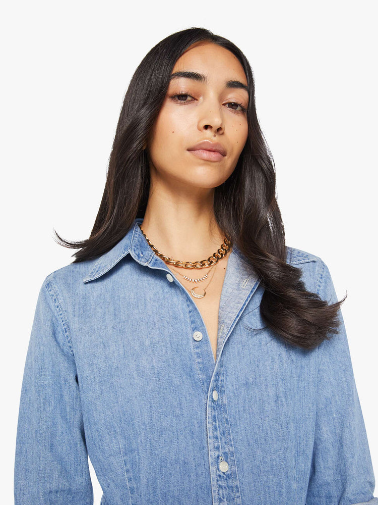 Close up view of a woman in a light blue denim button-up features curved hems and seamed details for a more narrow fit.