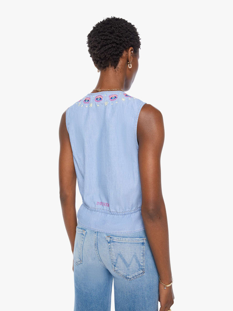 Back view of a woman in light blue with colorful embroidered eyes at the neckline denim tank with a crewneck, buttons down the front and a tie-waist detail.