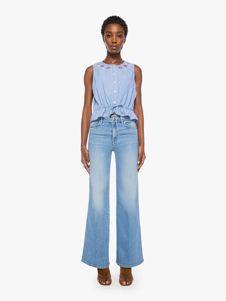 full body view of a woman in light blue with colorful embroidered eyes at the neckline denim tank with a crewneck, buttons down the front and a tie-waist detail.