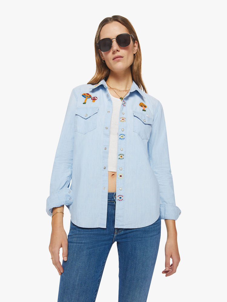 Front view of a western denim button up with front patch pockets, a curved hem, and snap closures down the front and at the wrists in a light blue with embroidery on chest and shoulders.