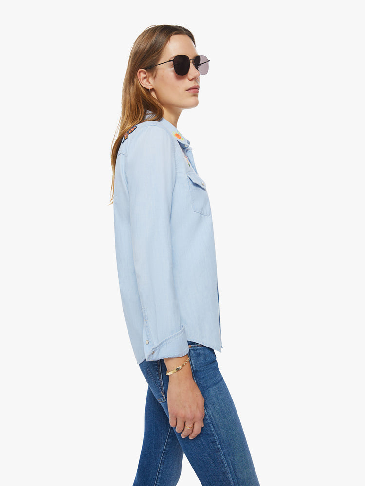 Side view of a western denim button up with front patch pockets, a curved hem, and snap closures down the front and at the wrists in a light blue with embroidery on chest and shoulders.