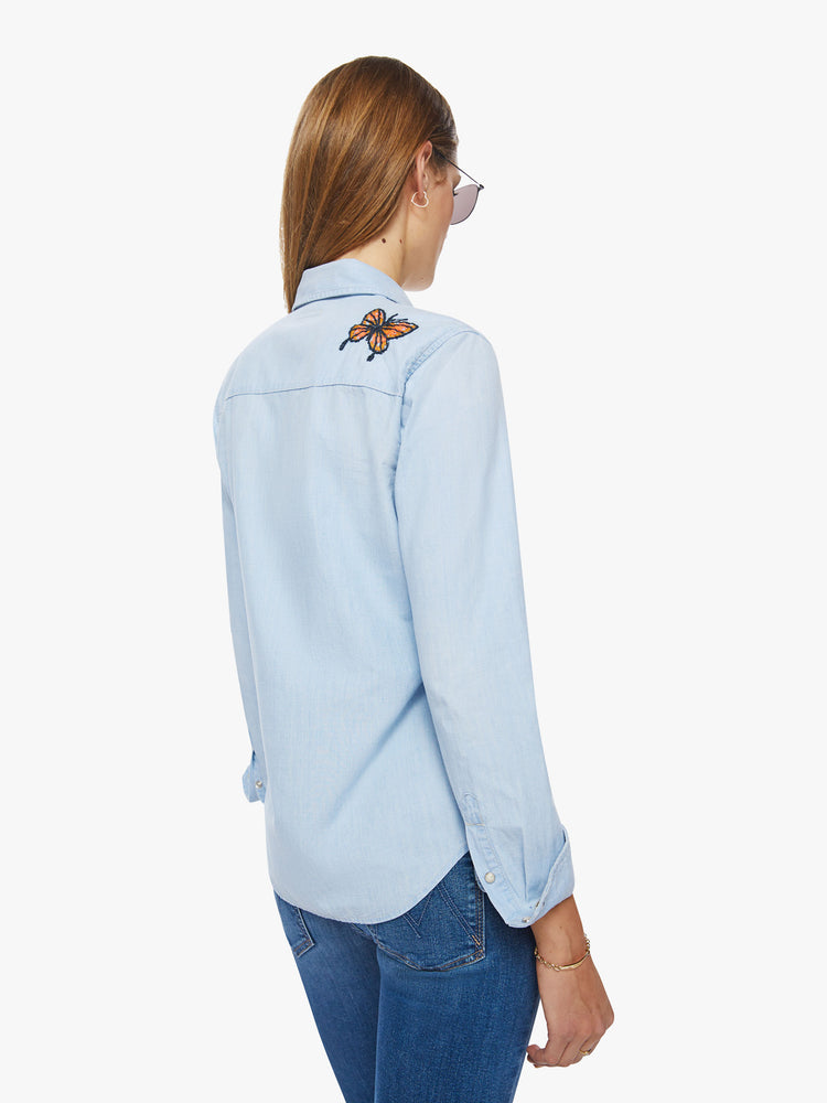 Back view of a western denim button up with front patch pockets, a curved hem, and snap closures down the front and at the wrists in a light blue with embroidery on chest and shoulders.