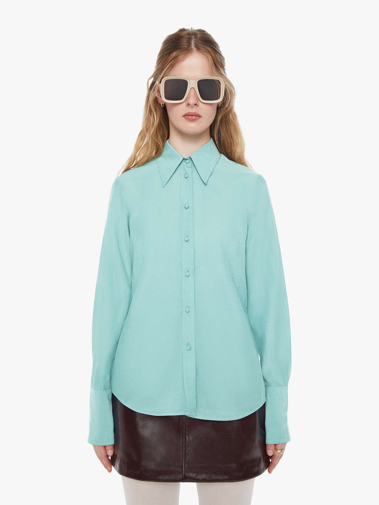 Front view of a woman in light turquoise blue button-up with a pointed collar, long balloon sleeves, extra-wide cuffs at the wrists.